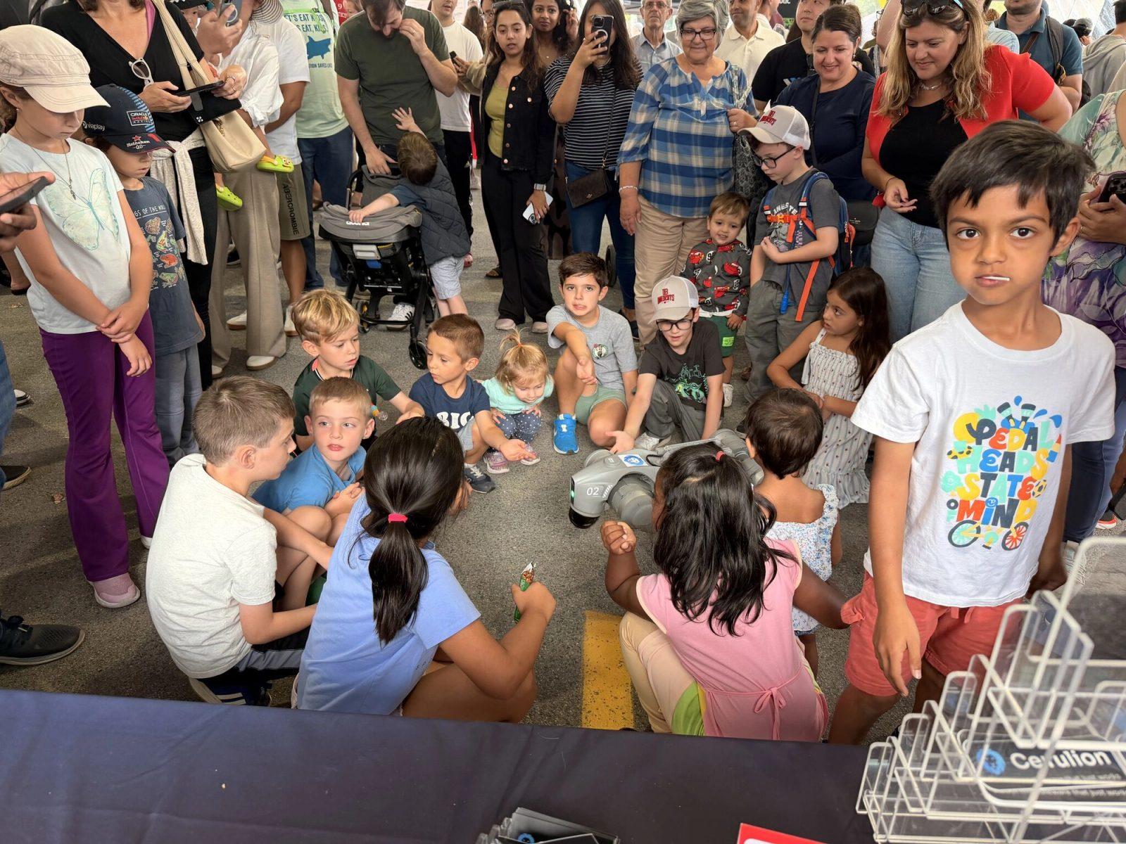 Children sit on the ground in front of the Cerulion booth at RoboBoston 2025