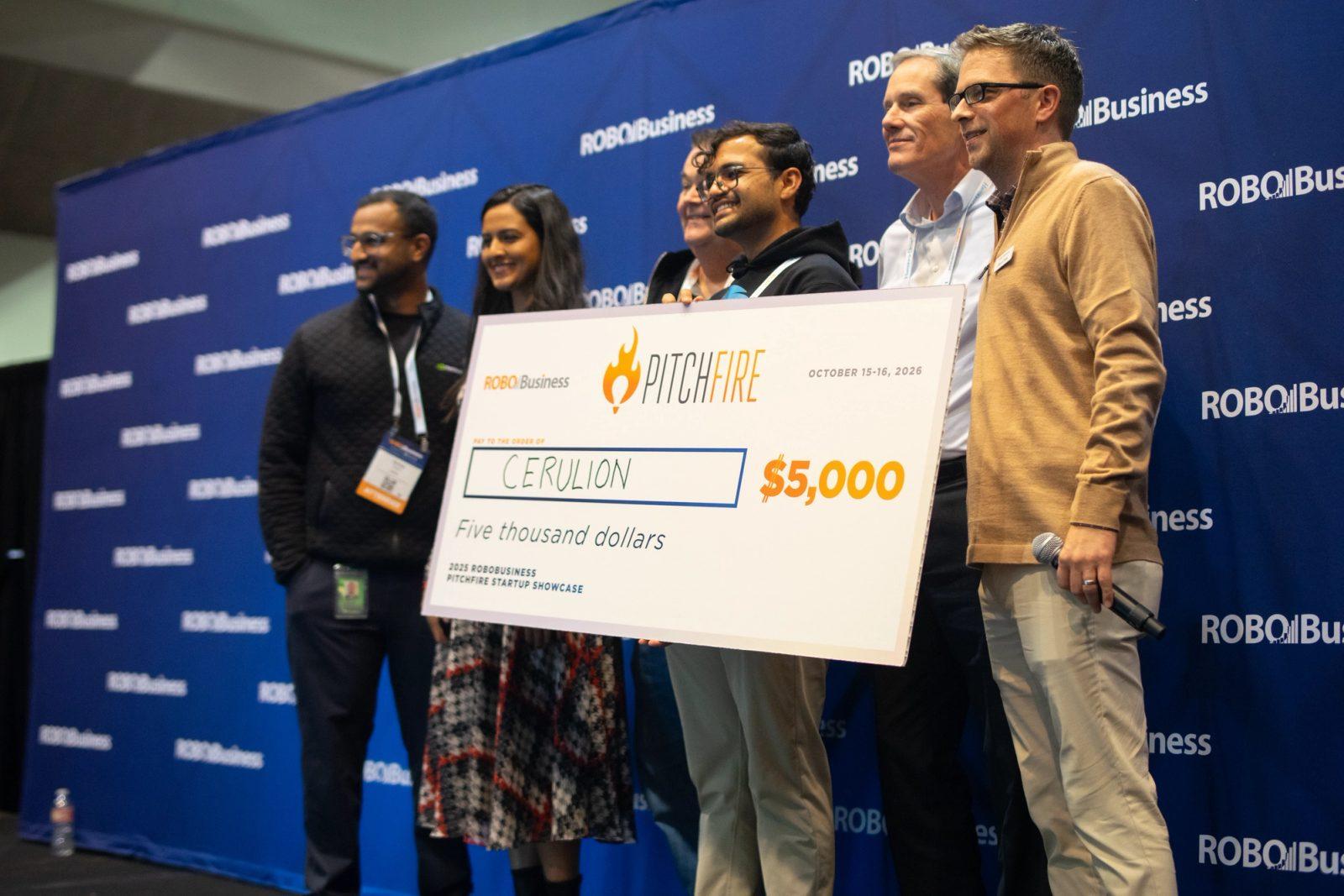 The Cerulion team holds the oversized $5,000 Pitchfire winner's check on the RoboBusiness stage